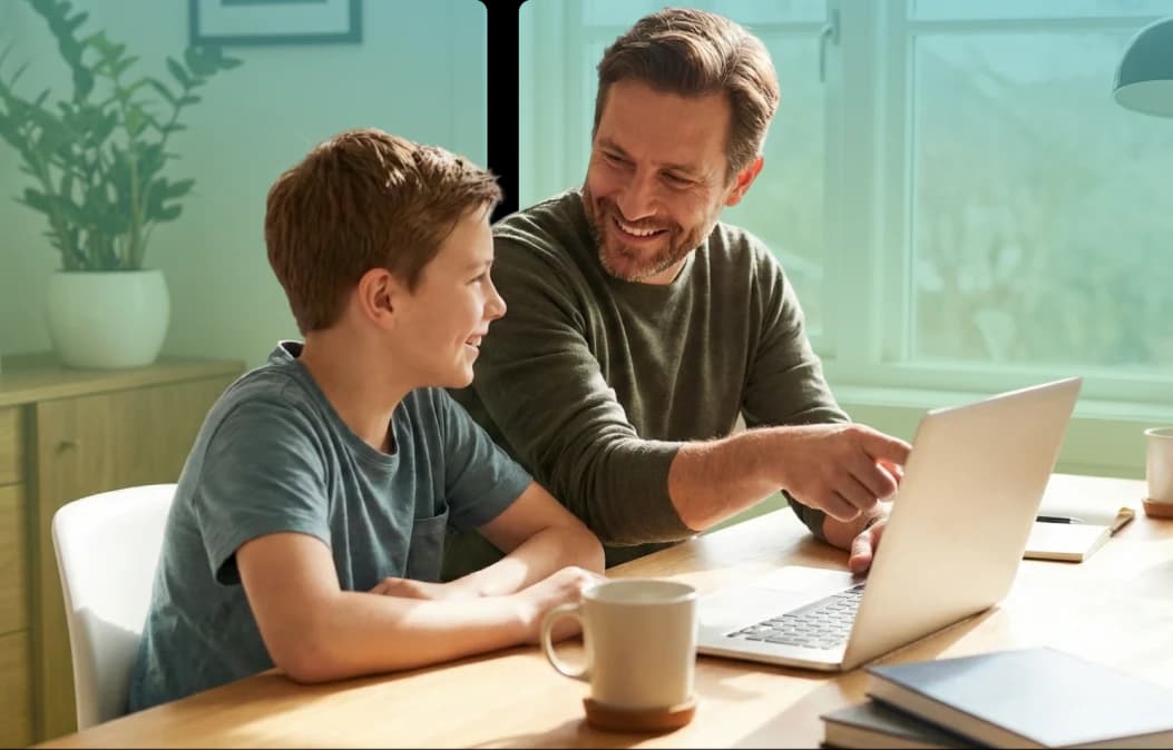 Menino e homem sorrindo sentados em frente a um laptop